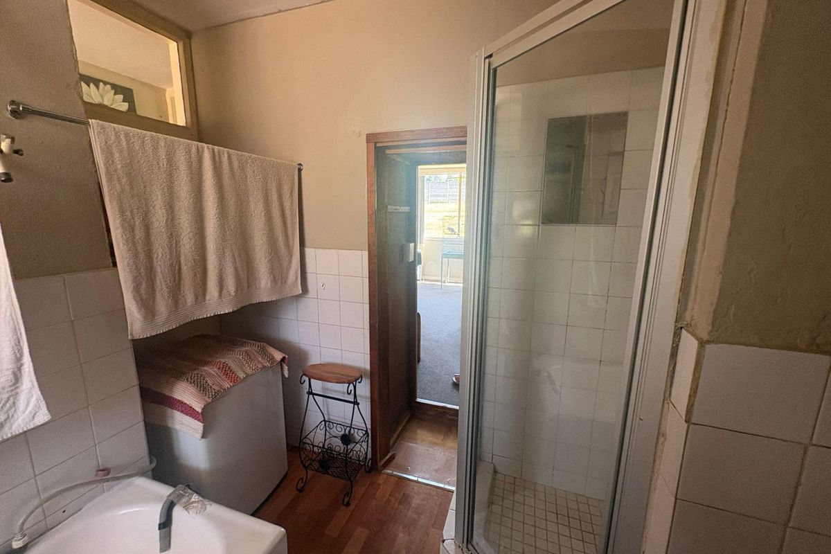 A functional bathroom featuring a shower enclosure, tiled wall finishes, and laminate flooring, requiring cosmetic updates to modernize the space.