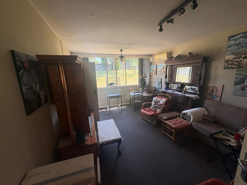 A living room featuring a ceiling fan, track lighting, and a wall-mounted air conditioning unit, with large windows providing natural light.