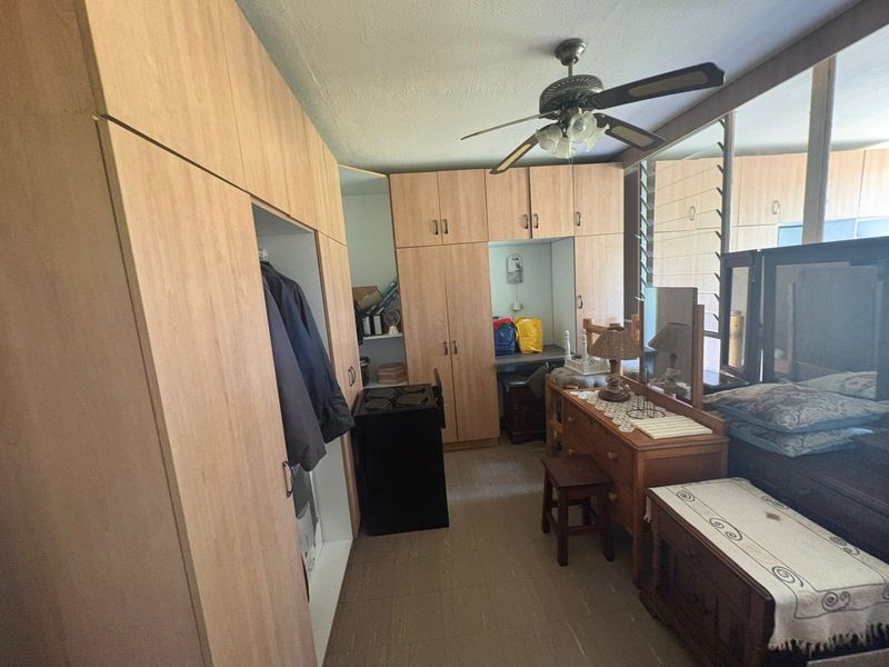 Bedroom featuring extensive built-in wooden cabinetry, mirrored wardrobe doors, and a ceiling fan, providing ample storage space.