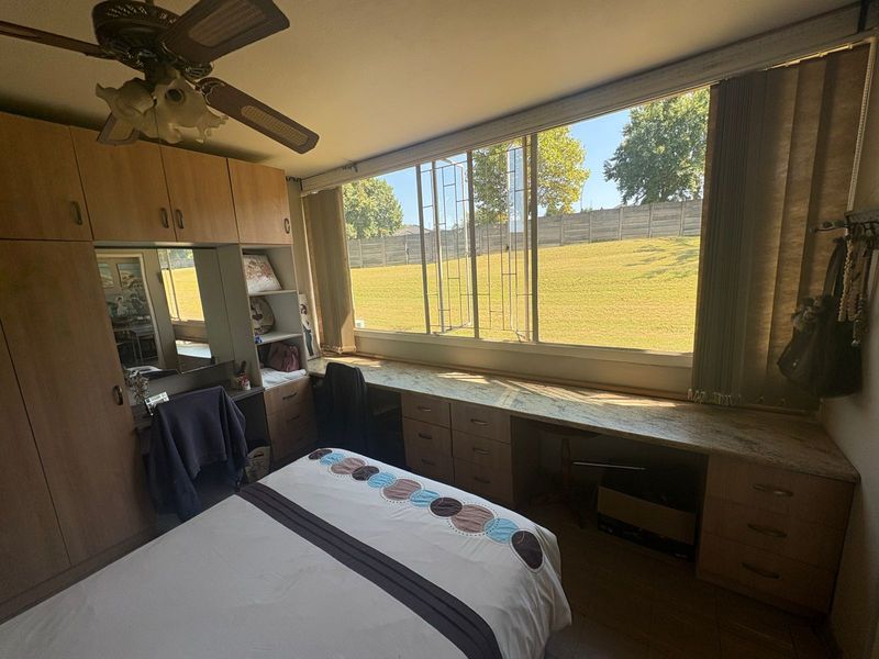 A bedroom featuring extensive built-in cabinetry, a desk area, and a large window overlooking a grassy outdoor space.