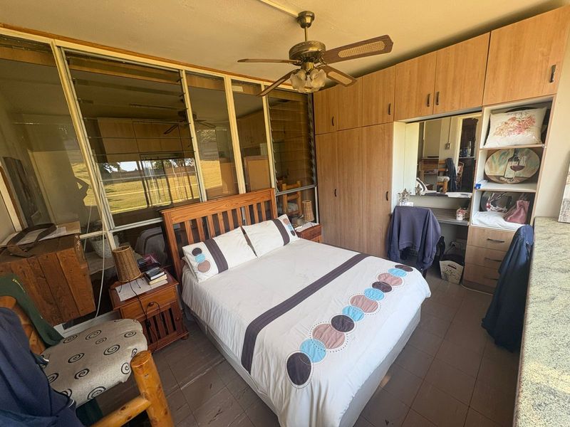 Bedroom featuring built-in wooden cupboards, a ceiling fan, and louver windows, offering a functional space with potential for modern updates.