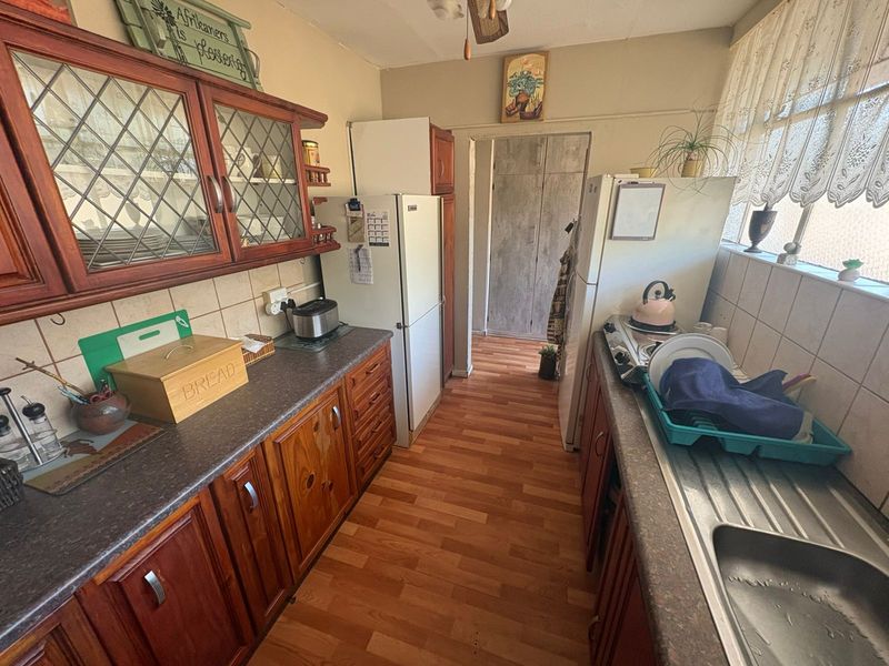 A functional kitchen featuring wooden cabinetry, laminate countertops, a stainless steel sink, and tiled backsplash, offering potential for a modern renovation.