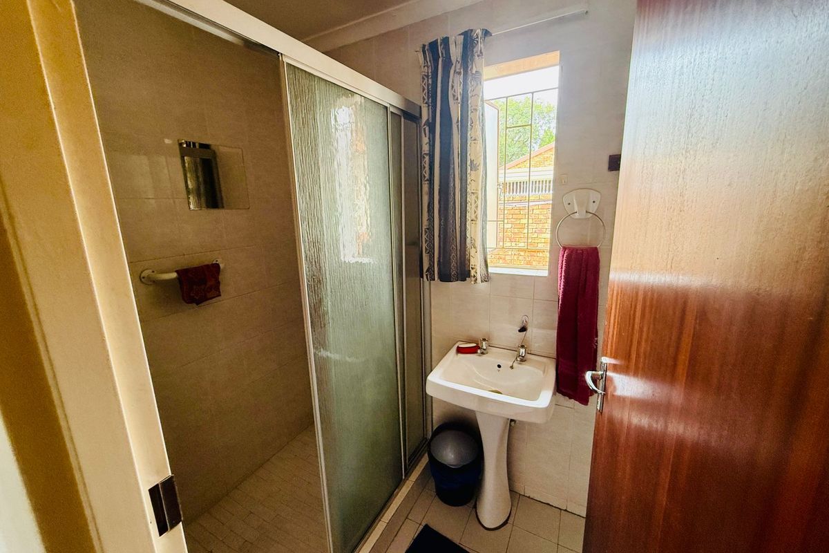 A functional bathroom featuring a glass-enclosed shower, a pedestal basin, and tiled flooring, providing essential amenities in a compact layout.