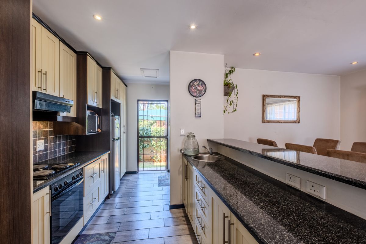 A well-appointed kitchen featuring granite countertops, built-in cabinetry, an electric stove with extractor, and a breakfast bar overlooking the adjacent living area.