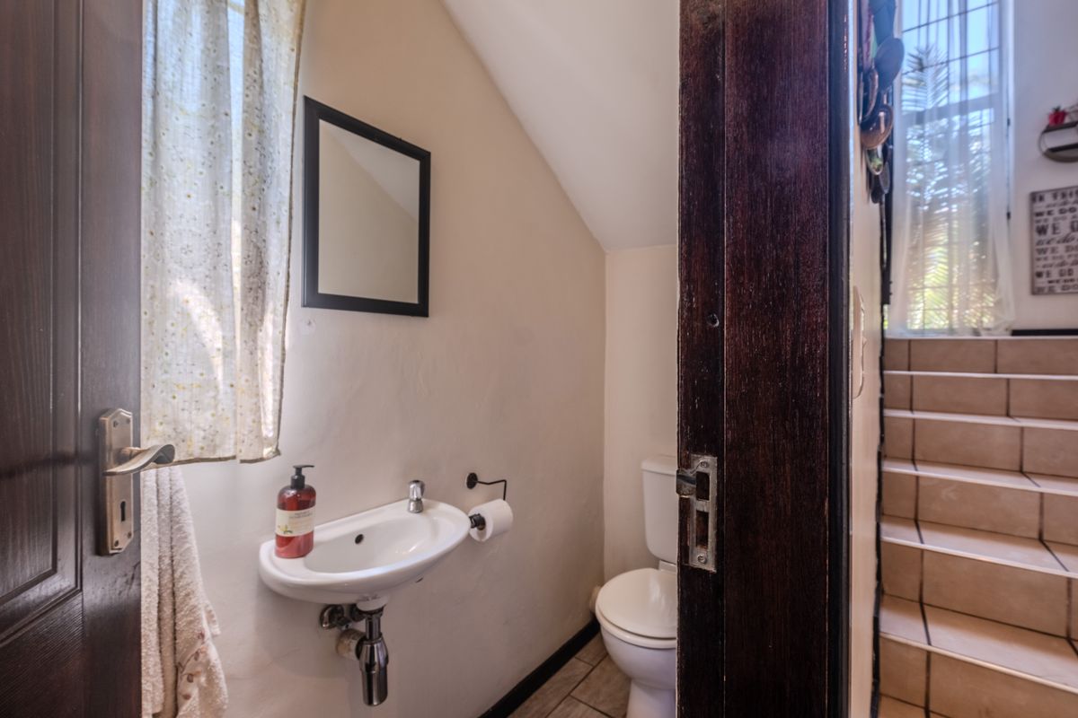 A compact guest bathroom featuring a wall-mounted basin and toilet, with tiled flooring and direct access to a staircase area.