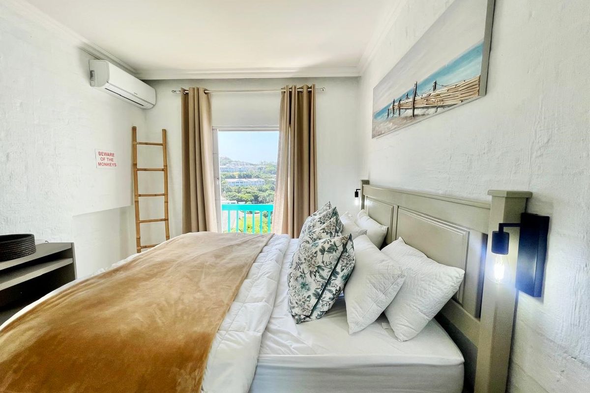A bright bedroom featuring a wall-mounted air conditioning unit, built-in headboard, and direct access to a balcony with scenic views.