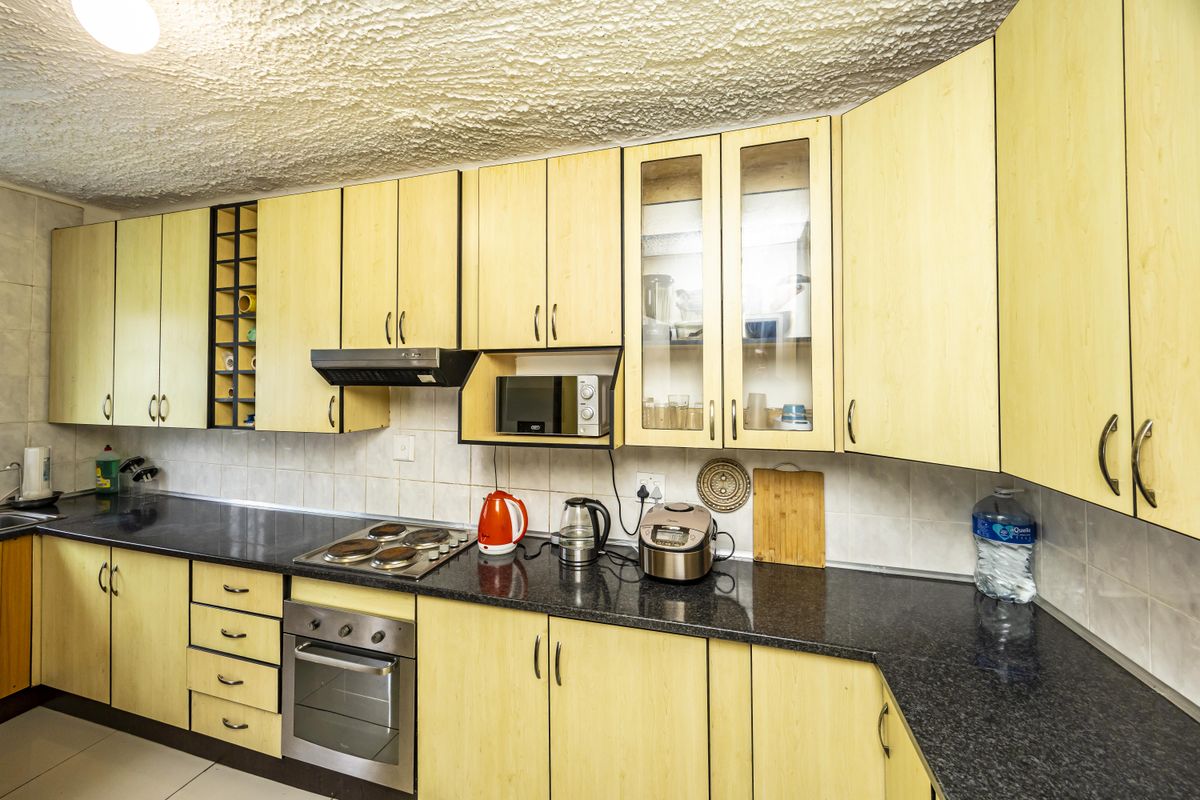 A functional kitchen featuring light wood-finish cabinetry, dark granite countertops, a built-in oven, and a hob with an extractor fan.