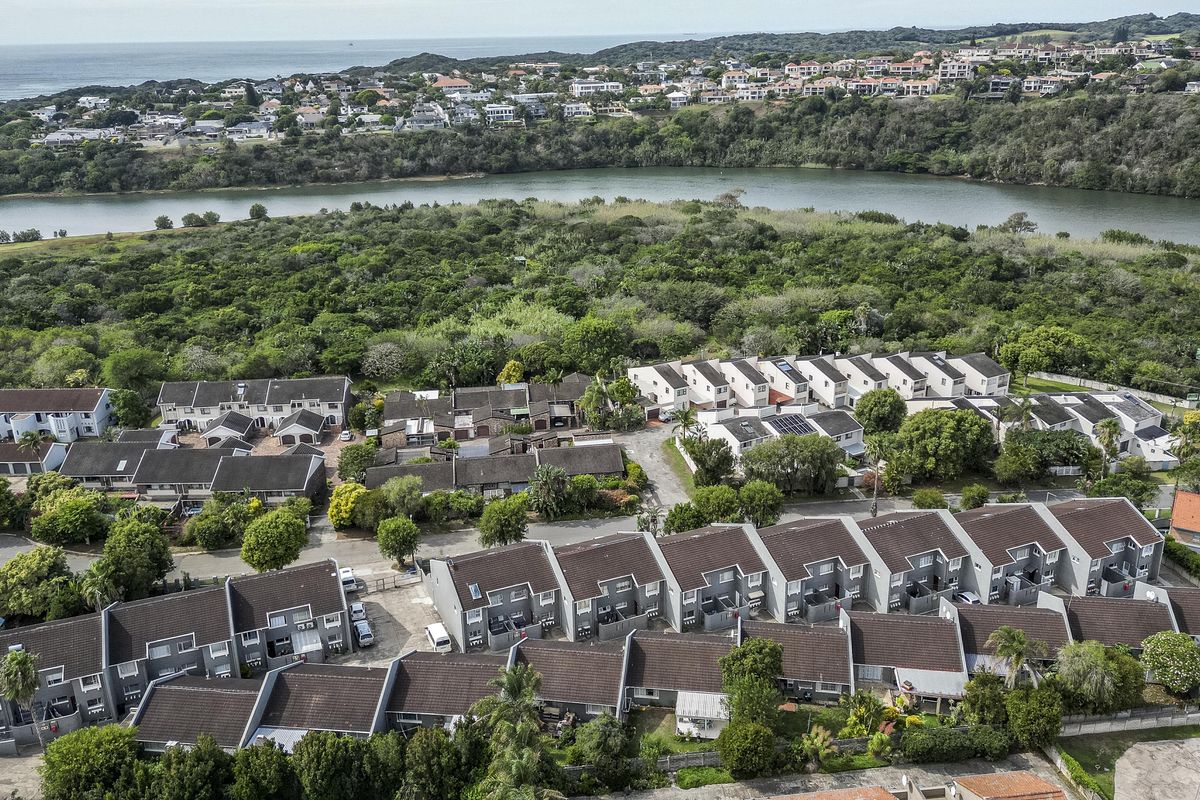 Aerial view of a townhouse complex featuring multiple residential units with tiled roofs, situated near a river and coastal landscape.