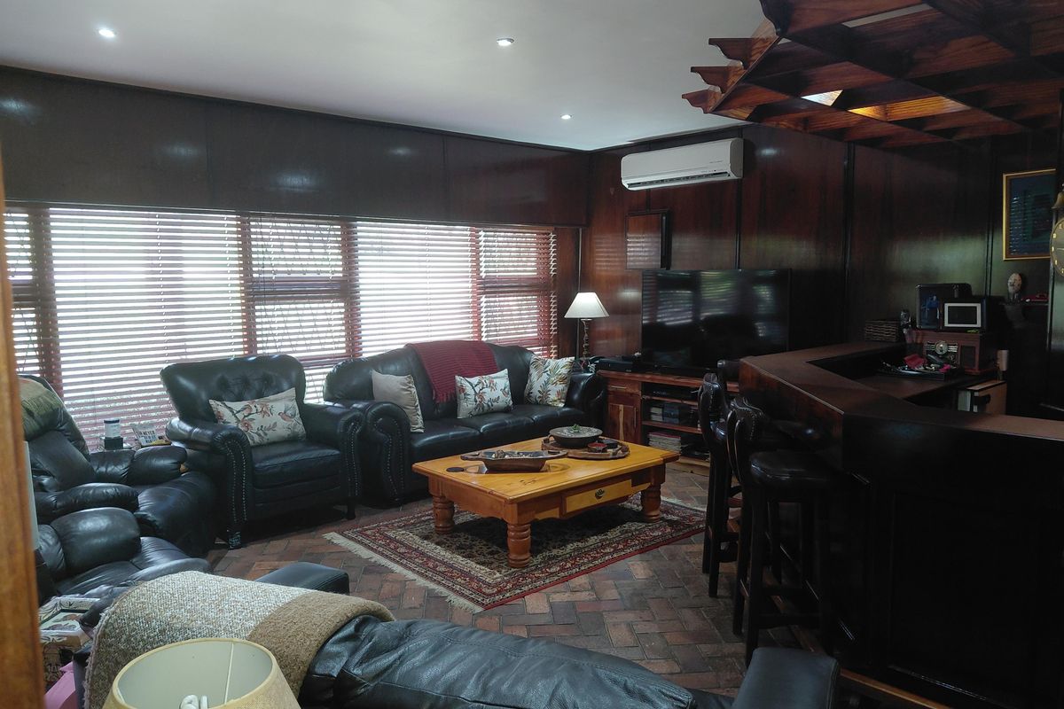 Spacious living room featuring dark timber wall paneling, a built-in bar, brick flooring, and a decorative timber ceiling feature with integrated lighting.