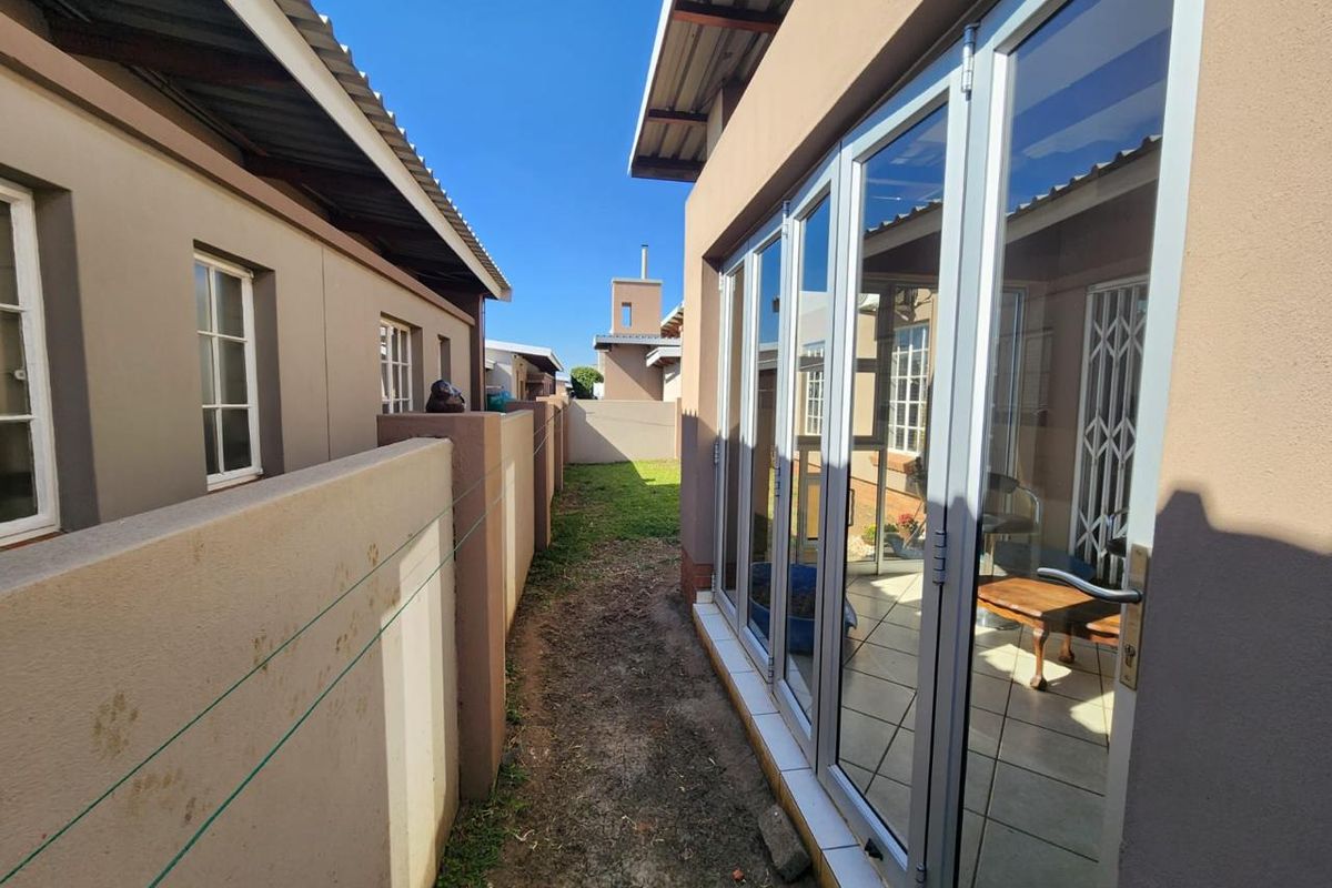 A side exterior view of the townhouse featuring a narrow garden strip and modern aluminium folding glass doors leading into the living area.
