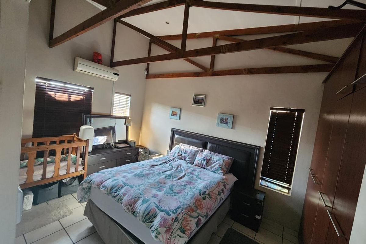 Spacious bedroom featuring high vaulted ceilings with exposed timber trusses, tiled flooring, built-in cabinetry, and a wall-mounted air conditioning unit.