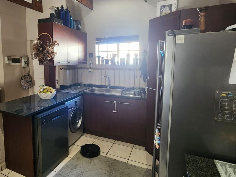 Compact kitchen featuring dark wood cabinetry, granite countertops, double basin sink, and integrated space for laundry appliances.