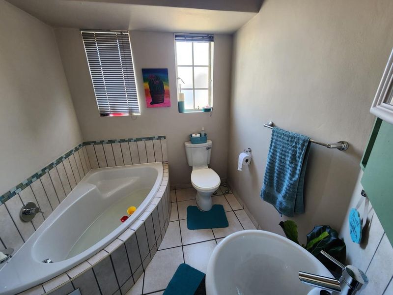 A functional bathroom featuring a corner bathtub with tiled surround, a standard toilet, and a pedestal basin with chrome fixtures.