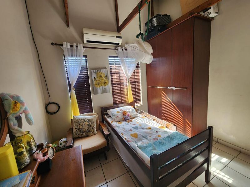 A bedroom featuring a vaulted ceiling, tiled flooring, built-in wardrobe, and a wall-mounted air conditioning unit.