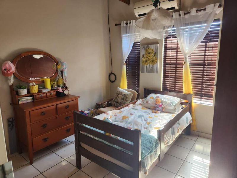 A bedroom featuring tiled flooring, wooden window blinds, and a wall-mounted air conditioning unit.