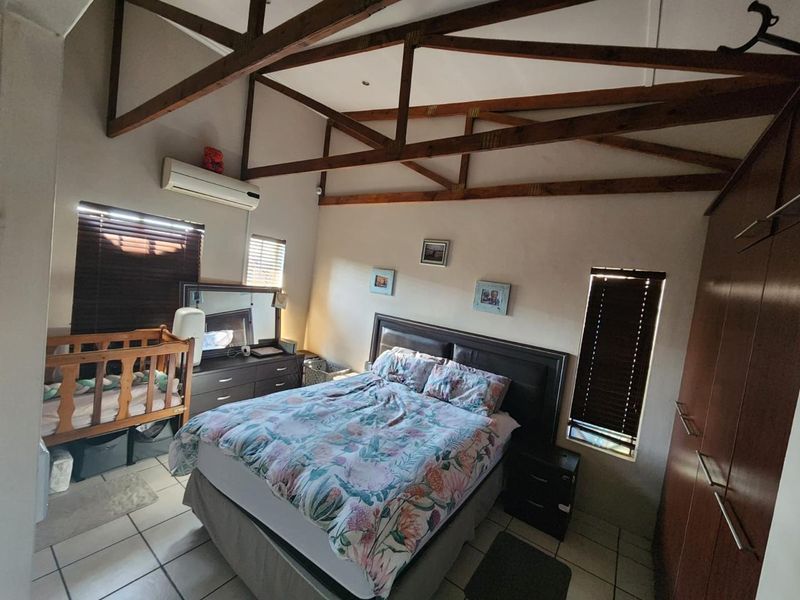 Spacious bedroom featuring high vaulted ceilings with exposed timber trusses, tiled flooring, built-in cabinetry, and a wall-mounted air conditioning unit.