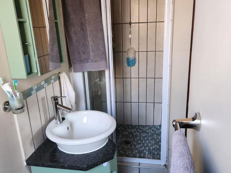 Compact bathroom featuring a corner vanity with vessel sink, wall-mounted mirror cabinet, and a tiled shower enclosure.