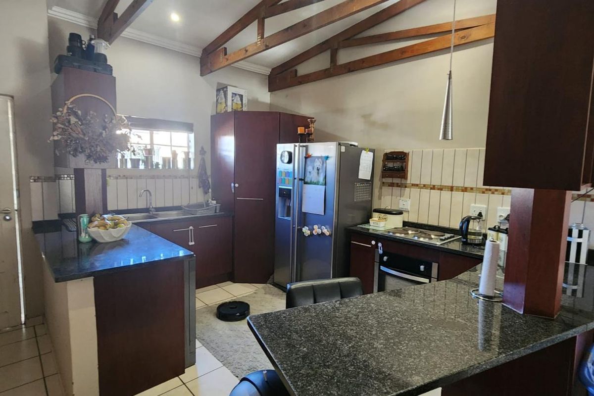 A functional kitchen featuring dark wood cabinetry, granite countertops, a built-in oven and hob, and exposed timber roof trusses.