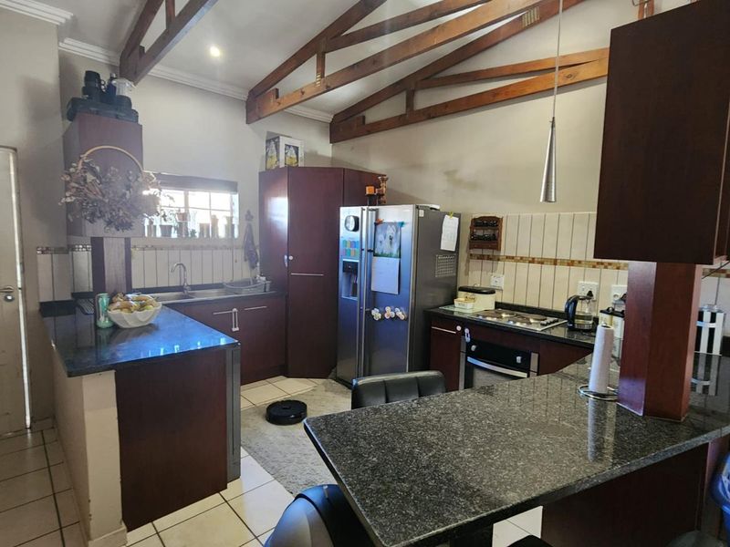 A functional kitchen featuring dark wood cabinetry, granite countertops, a built-in oven and hob, and exposed timber roof trusses.