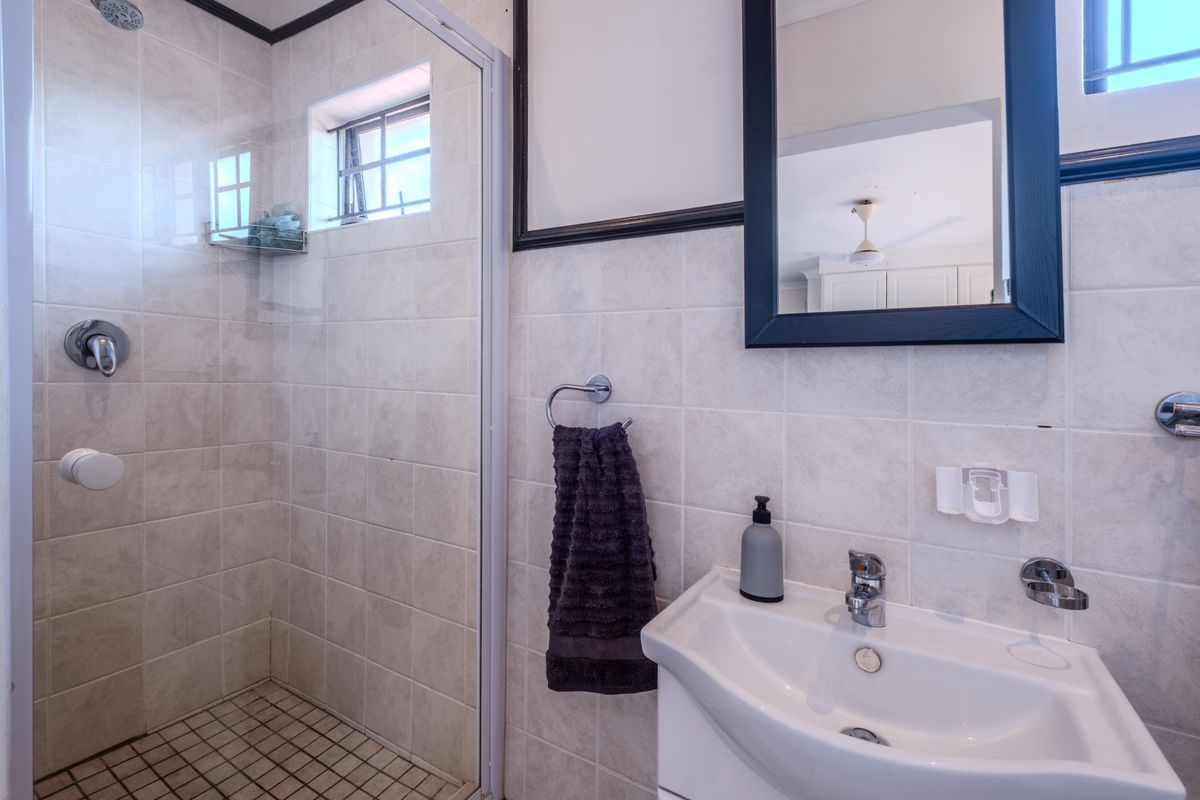 A functional bathroom featuring a tiled shower enclosure, wall-mounted basin, and neutral wall tiling, providing a clean and practical space.