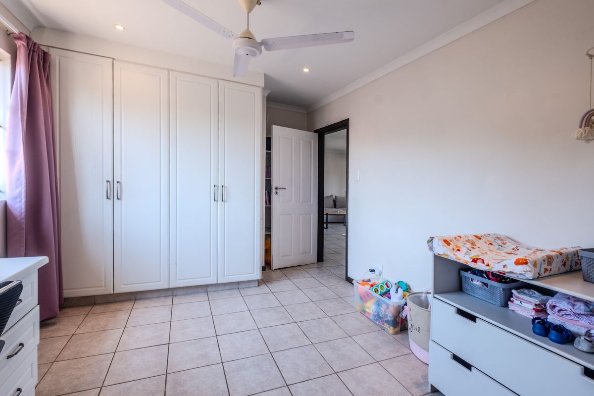 A well-lit bedroom featuring neutral tiled flooring, ample built-in cupboard storage, and a ceiling fan, offering a clean and functional living space.