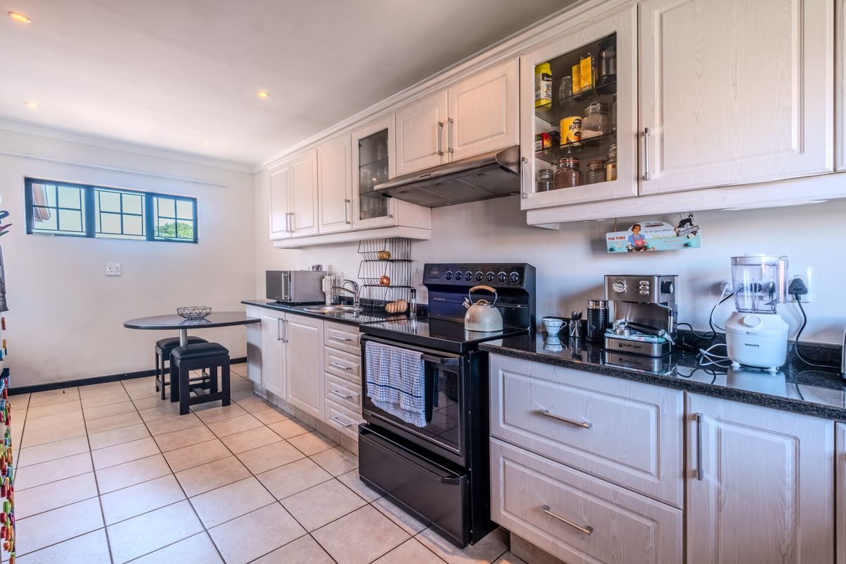 A well-maintained kitchen featuring light-toned cabinetry, granite countertops, tiled flooring, and a freestanding stove with an integrated extractor fan.