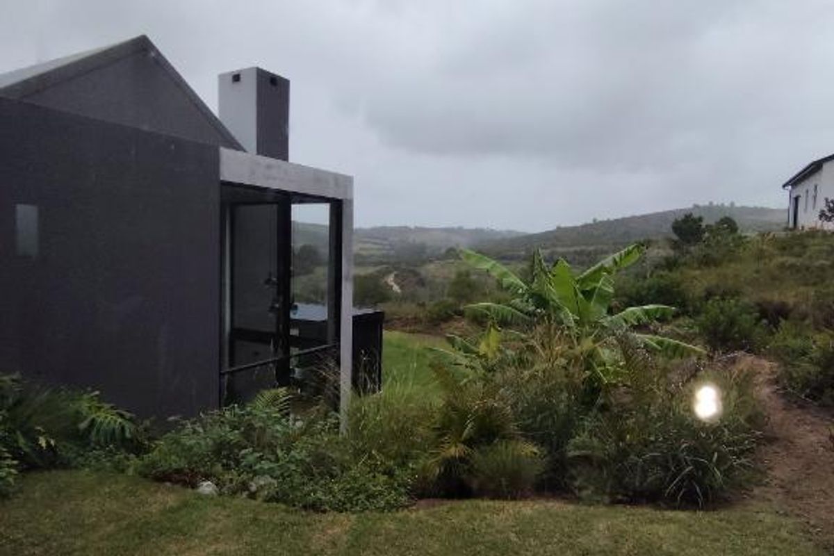 A modern architectural home exterior featuring a concrete chimney and landscaped garden with scenic rolling hill views.
