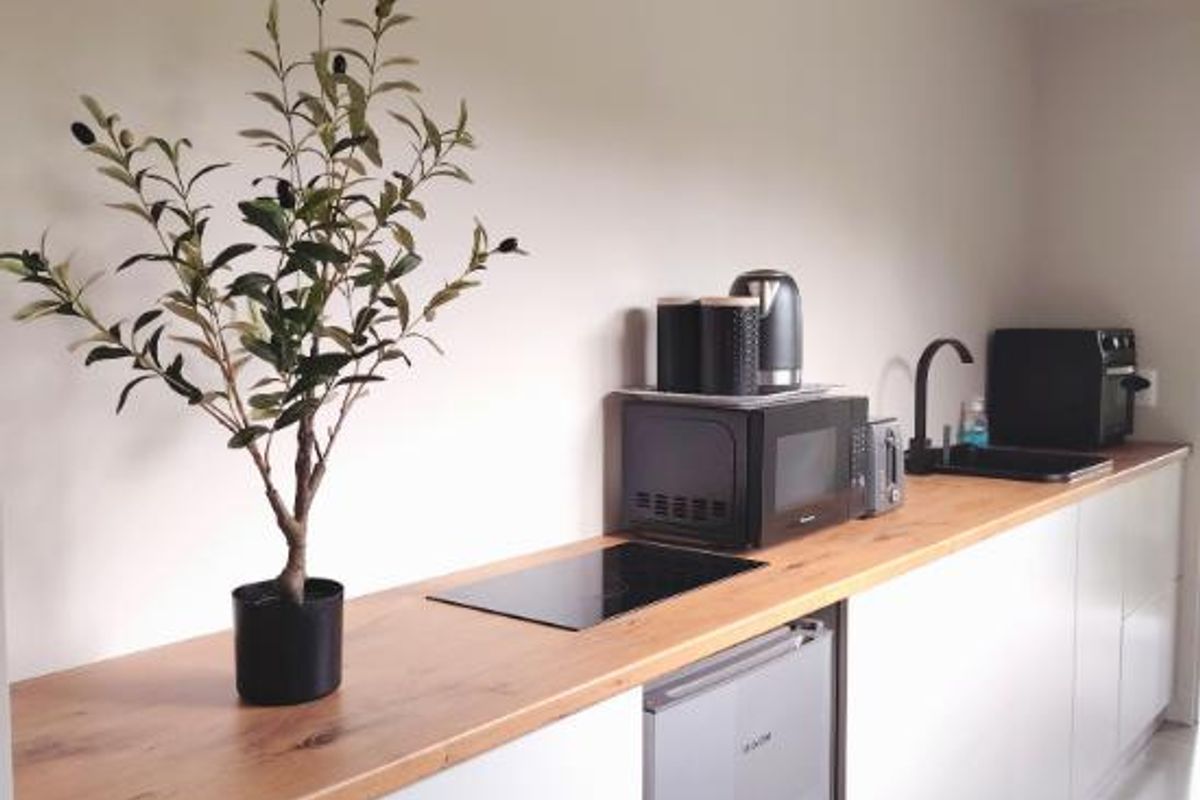 A modern, compact kitchen featuring sleek white cabinetry, a warm wooden countertop, an induction cooktop, and a black faucet with an integrated sink.