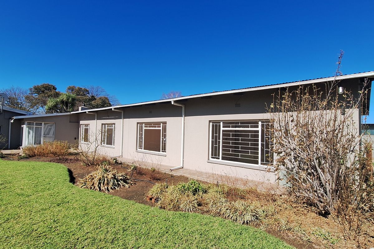 A view of the rear exterior of the house, featuring a lawn, garden beds, and multiple windows with security bars.