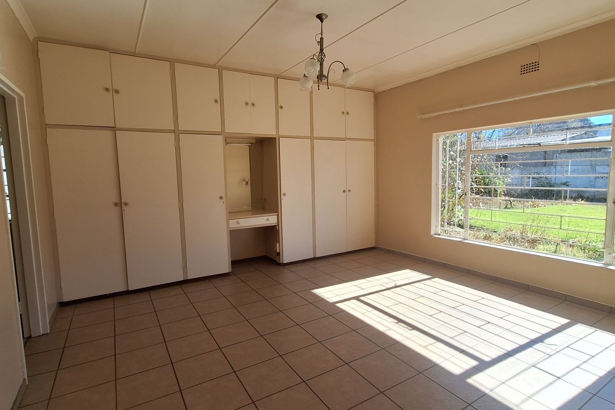 A spacious bedroom featuring extensive built-in cabinetry with a central vanity area, large windows, and tiled flooring.