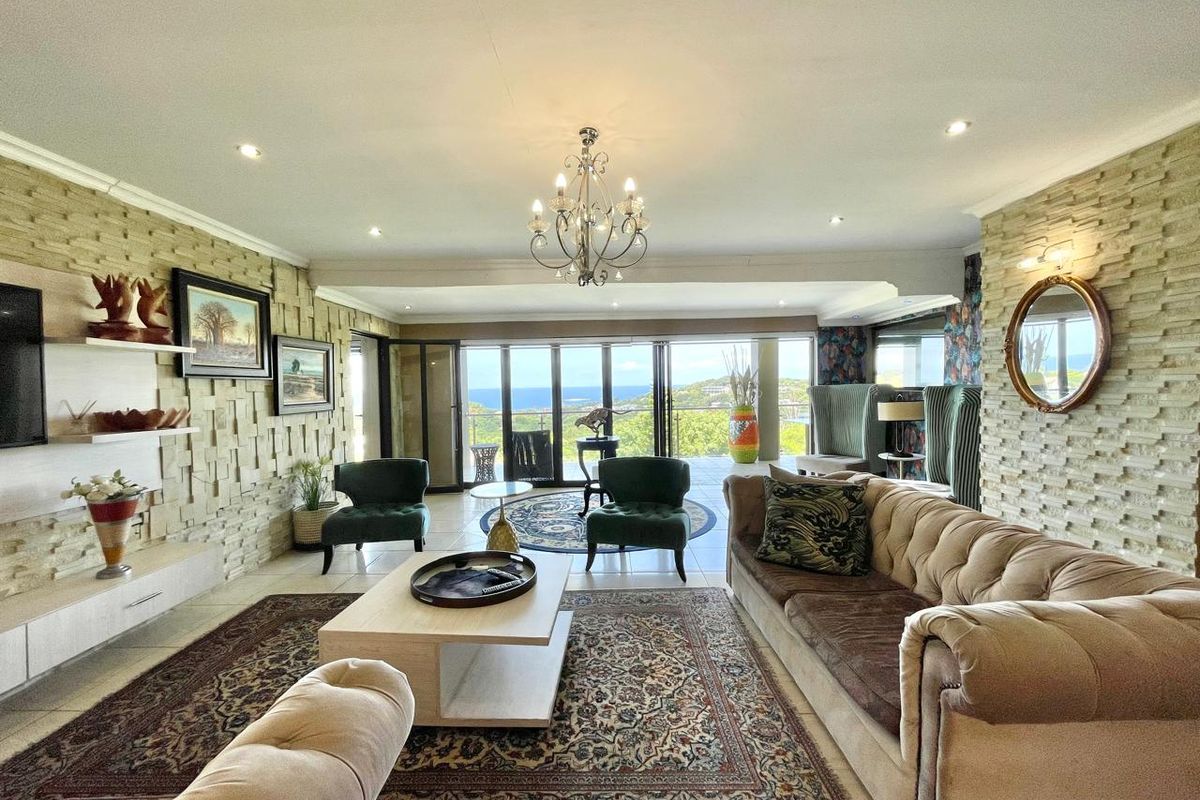 Spacious living room featuring textured stone feature walls, recessed downlighting, a decorative chandelier, and large sliding glass doors opening to a scenic outdoor view.