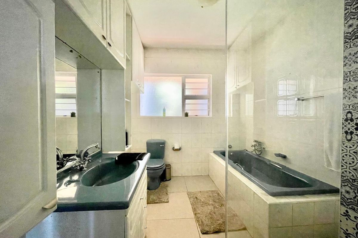 A functional bathroom featuring a built-in vanity with integrated sink, a bathtub with glass screen, and a toilet.