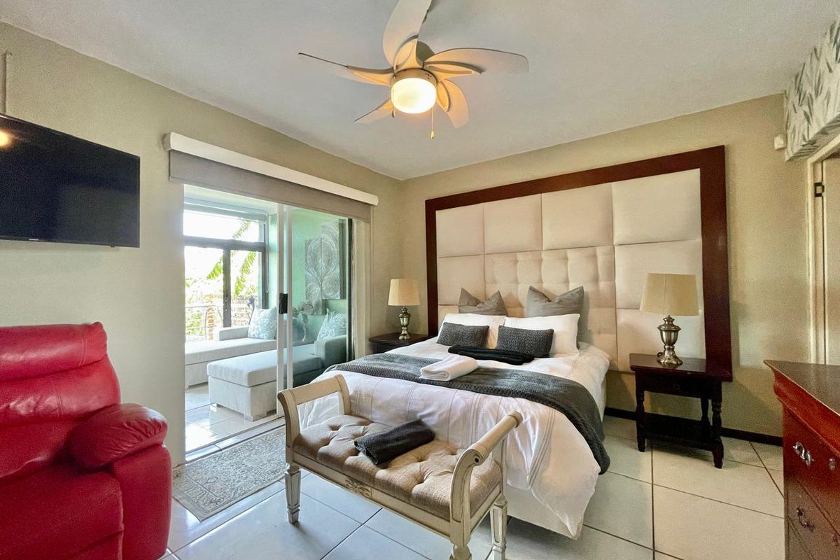 A well-lit bedroom featuring a large upholstered headboard, ceiling fan, and sliding glass doors providing direct access to an adjoining balcony.