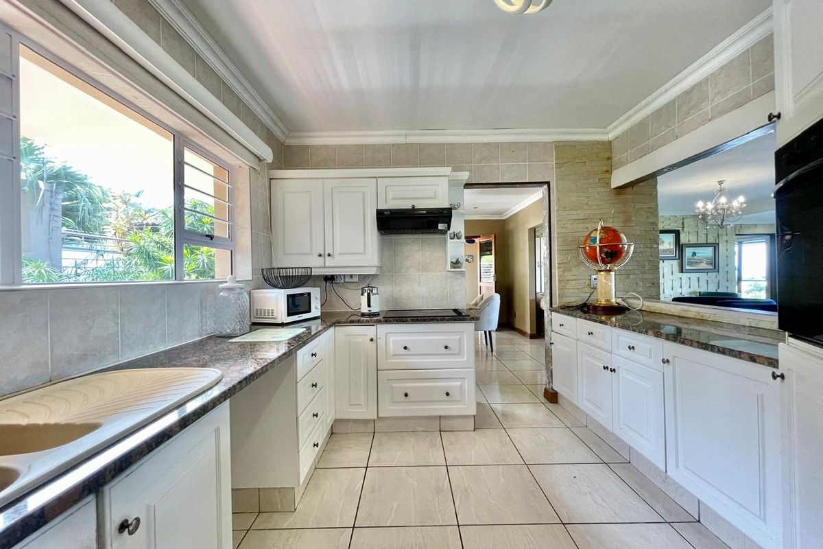 A functional kitchen featuring white cabinetry, granite-style countertops, tiled flooring, and a large window providing natural light and garden views.