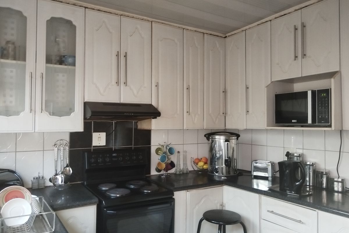 A functional kitchen featuring white cabinetry, dark countertops, a built-in microwave, and an electric stove with an extractor fan.