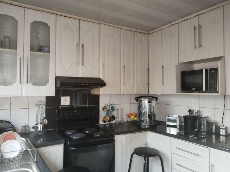 A functional kitchen featuring white cabinetry, dark countertops, a built-in microwave, and an electric stove with an extractor fan.