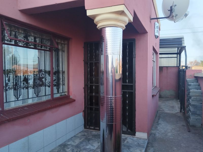 Front entrance area featuring a tiled porch, decorative column, and security gates, with visible wear to the exterior wall finishes.
