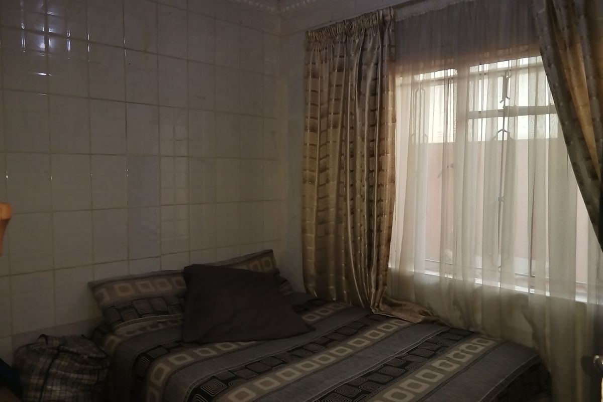 A bedroom featuring tiled walls and a window with security bars, requiring cosmetic updates to improve the overall aesthetic and condition.