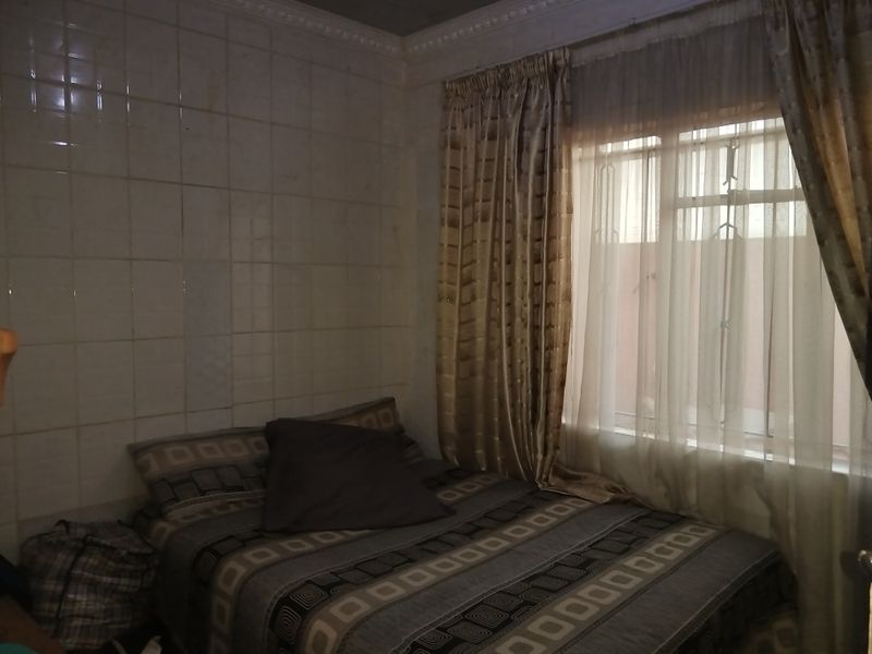 A bedroom featuring tiled walls and a window with security bars, requiring cosmetic updates to improve the overall aesthetic and condition.