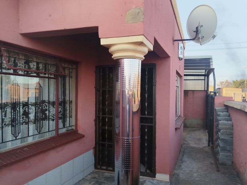 Front entrance area featuring a decorative column, security gates, and bars, with visible exterior wall maintenance required.