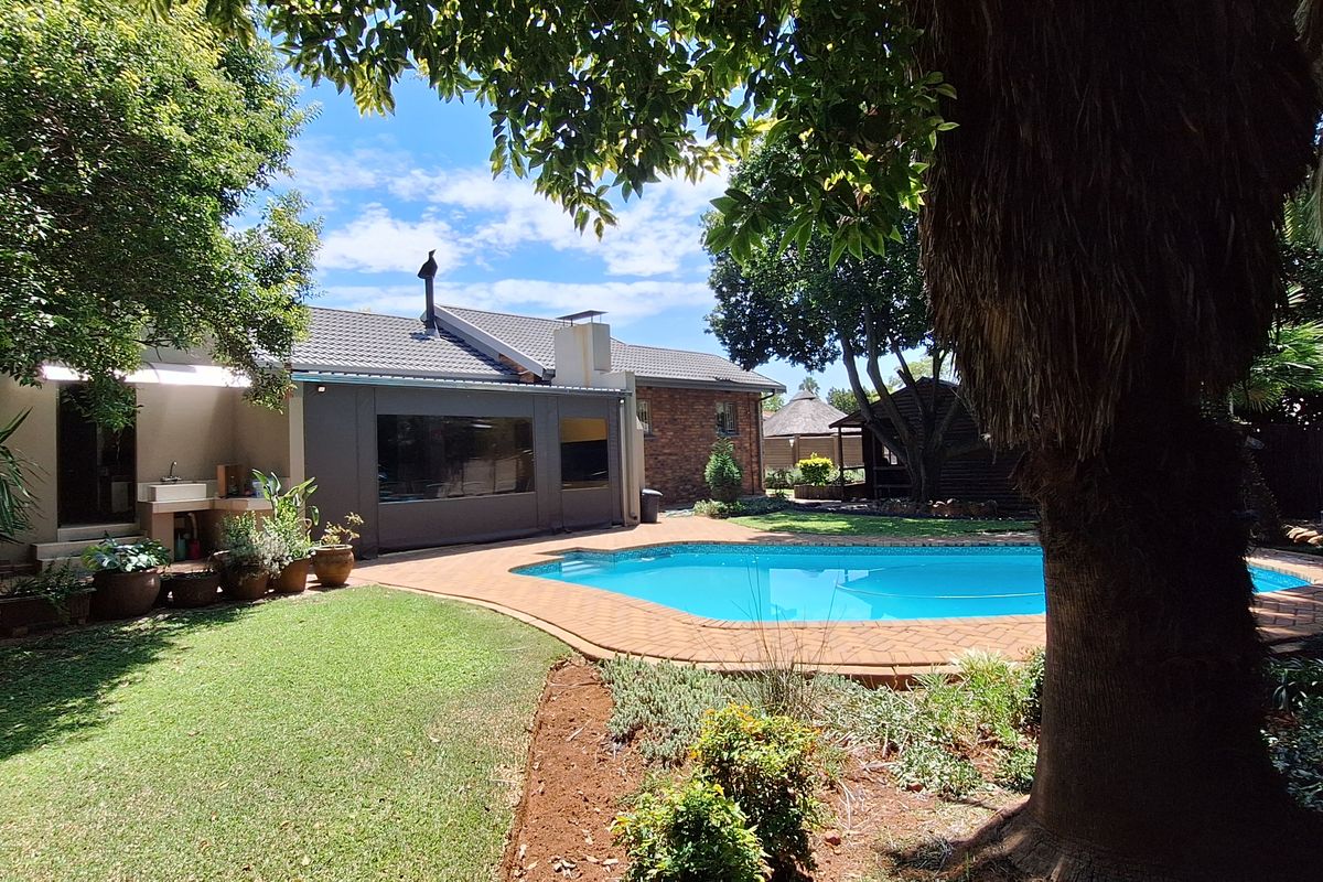 A well-maintained rear garden featuring a swimming pool with brick paving, established trees, and a covered patio area attached to the main house.