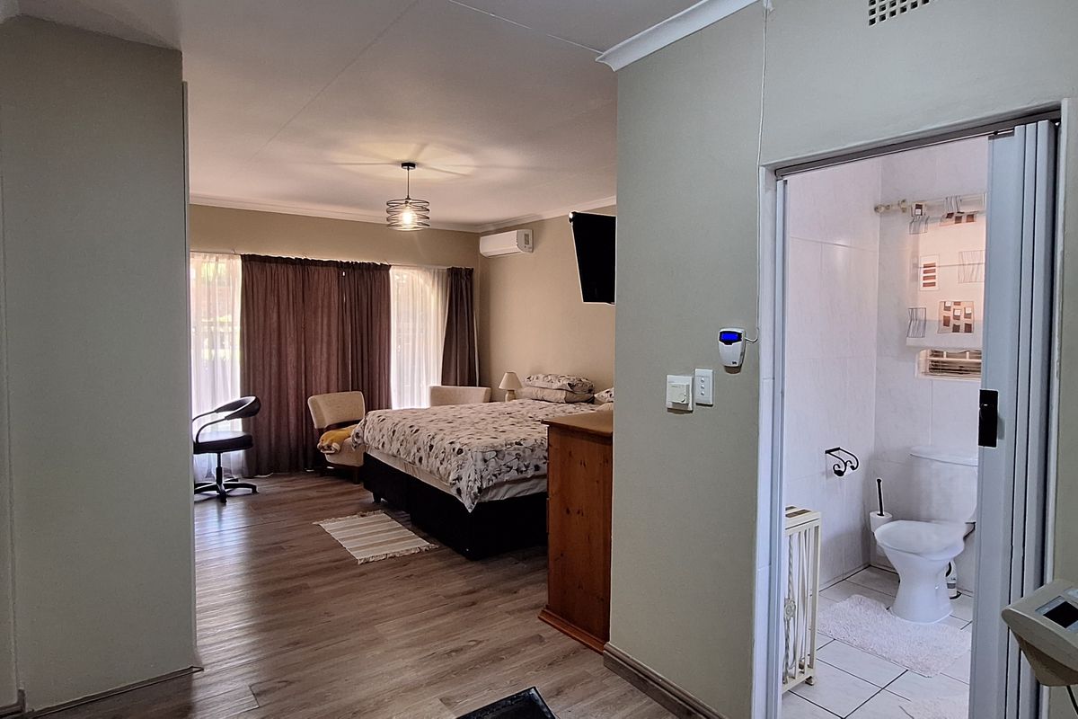 Spacious bedroom featuring wood-look flooring, an en-suite bathroom with tiled finishes, and a wall-mounted air conditioning unit.