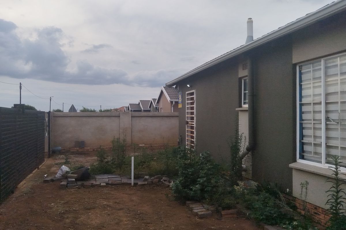 A view of the rear exterior of the property featuring a perimeter boundary wall, a side entrance, and an undeveloped garden space.