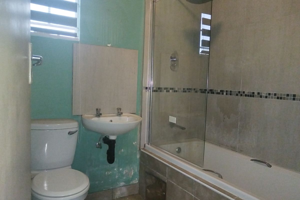 A functional bathroom featuring a bathtub with a glass shower screen, a wall-mounted basin, and a standard toilet.