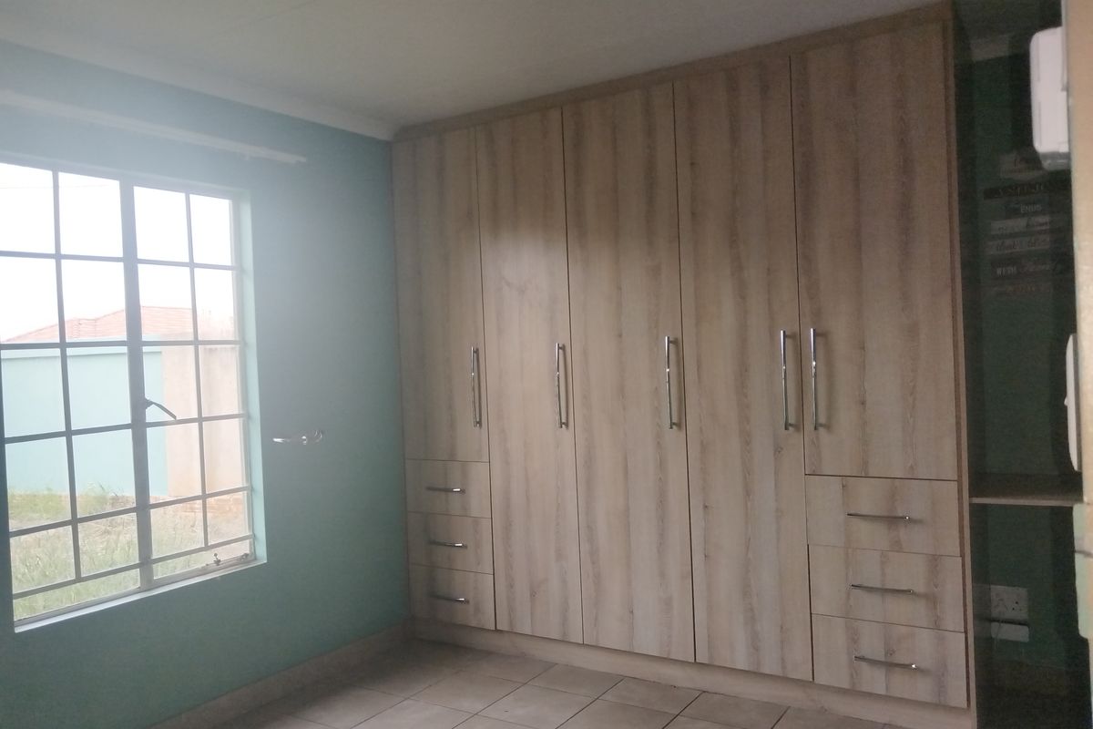 A bedroom featuring light wood-grain built-in cupboards with integrated drawers and tiled flooring, offering ample storage space.