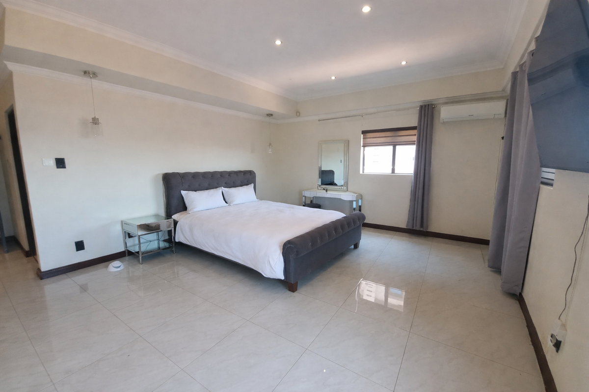 Spacious bedroom featuring neutral tiled flooring, recessed downlighting, and a wall-mounted split-system air conditioning unit.