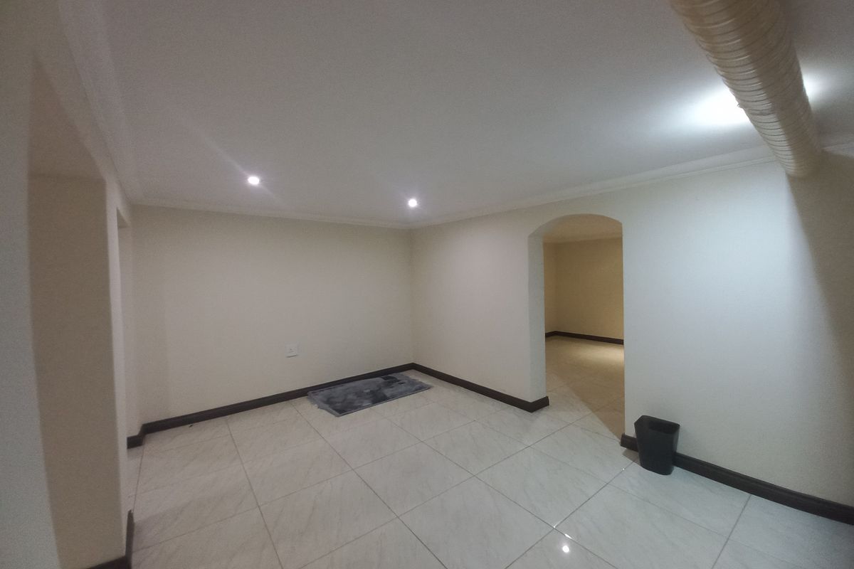 An empty, neutrally painted living area featuring tiled flooring, recessed downlighting, and an arched entryway leading to an adjacent space.