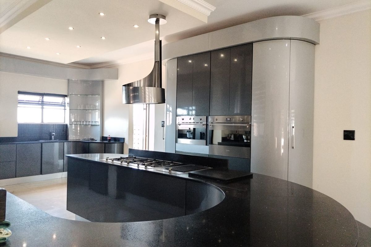 Modern kitchen featuring a distinctive curved island with granite countertops, high-gloss cabinetry, built-in double ovens, and a sleek stainless steel extractor hood.