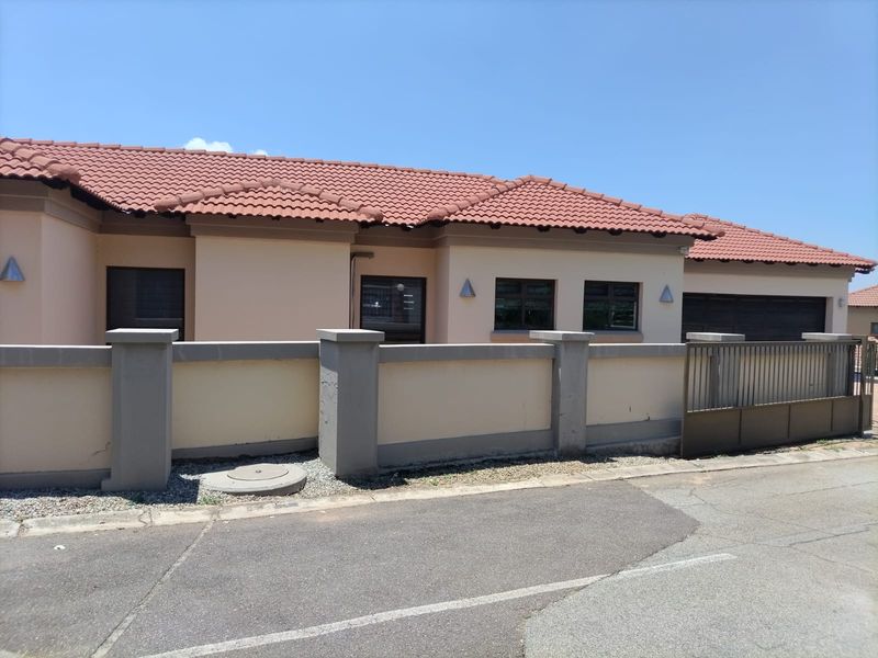 Front exterior view of a single-story house featuring a tiled roof, boundary wall with a sliding gate, and a garage.