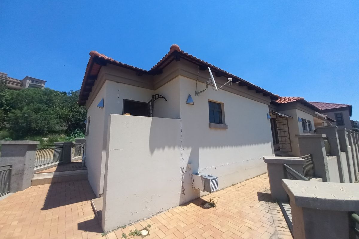 Rear exterior view of the property featuring paved walkways, terracotta roof tiles, and boundary walling with visible structural cracking on the exterior wall.